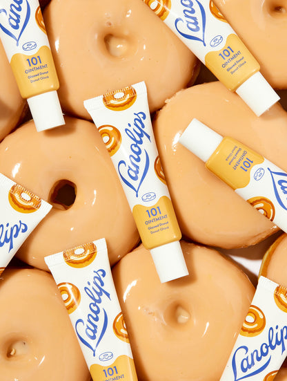 Flat lay of Lanolips 101 Ointment Multi-Balm in Glazed Donut, surrounded by glossy donuts. Made with lanolin, vitamin E and all-natural flavours, this cult-classic balm deeply hydrates and leaves lips soft, smooth.