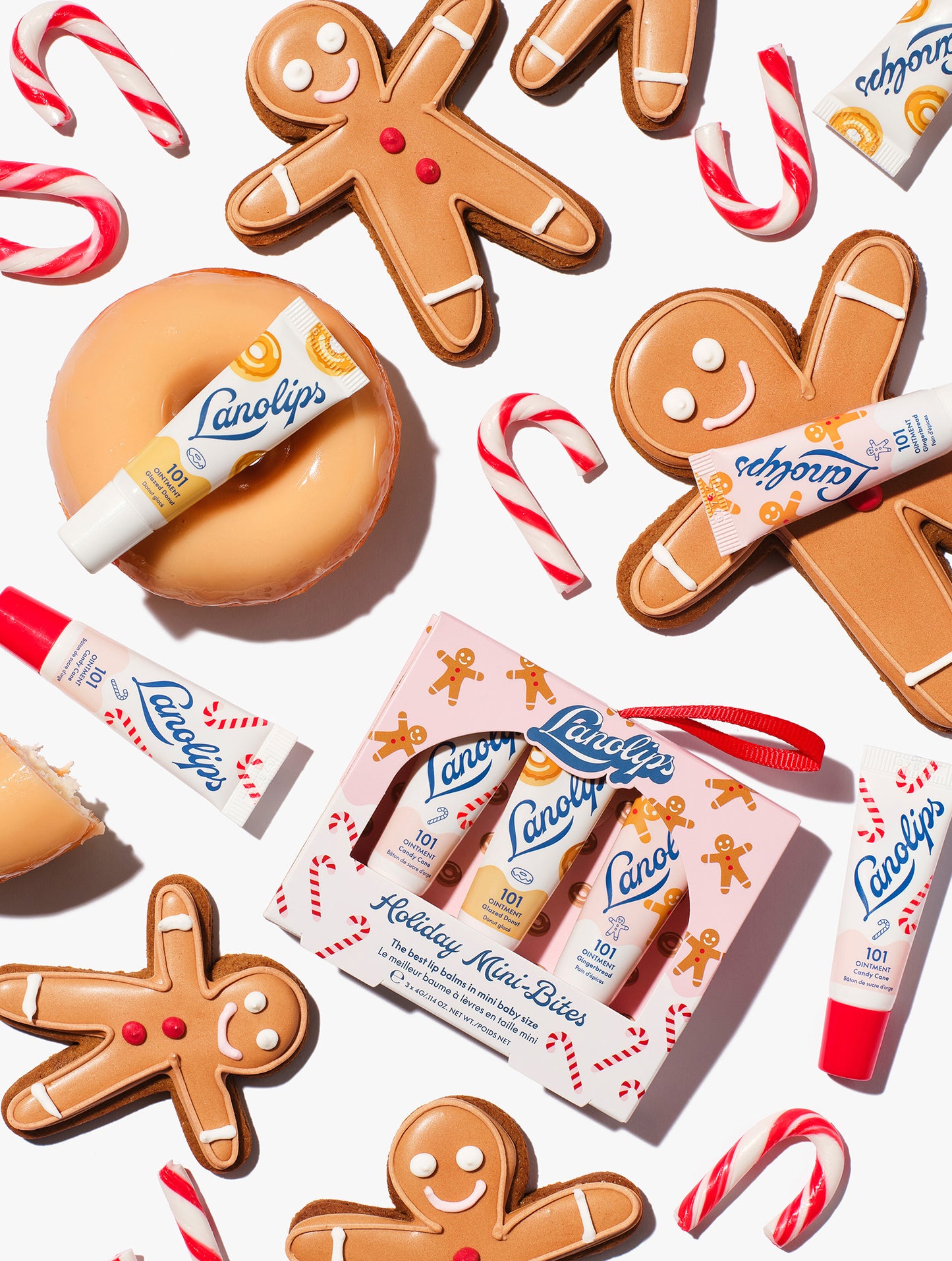 Flatlay of Lanolips Holiday Mini Bites lip balm trio gift set with Candy Cane, Gingerbread and Glazed Donut flavours, styled with gingerbread cookies and candy canes.