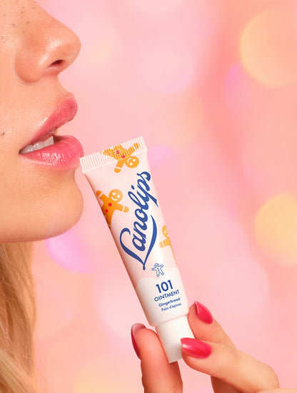 Model holding a tube Lanolips 101 Ointment Multi-Balm Gingerbread lip balm tube against a pink background.