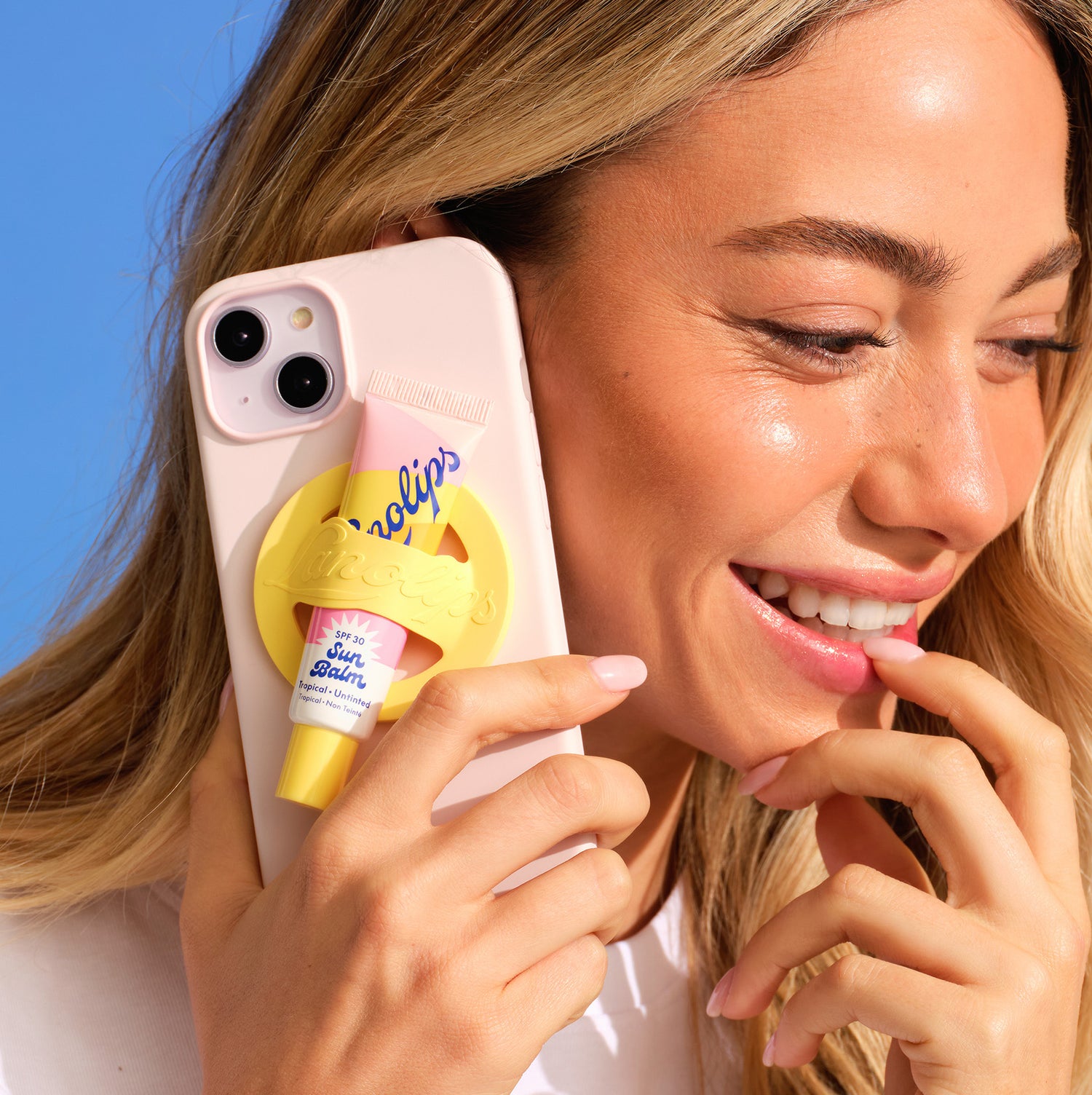 Model holding a Lanolips yellow phone lip holder with a yellow holder featuring the Lanolips Sun Balm SPF 30 Tropical Lip Balm against their face.