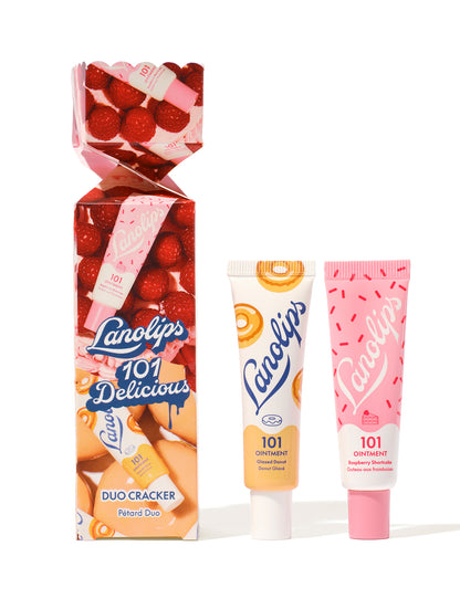 Still shot Lanolips 101 Delicious Holiday Duo Cracker, with the 101 Ointment Multi-Balms Glazed Donut and Raspberry Shortcake on the side of the cracker. 